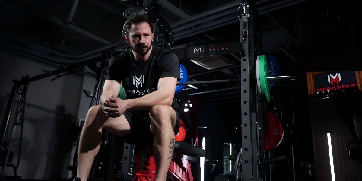 Recovery training for Home Gym Athletes: man sitting on a bench, resting between sets in a well-equipped home gym.