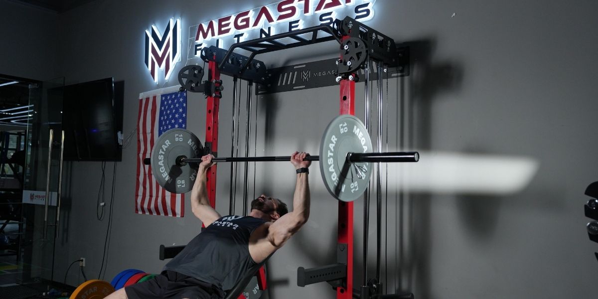 Man performing an incline bench press on a smith machine, lifting a barbell with gray plates at a Megastar Fitness gym.