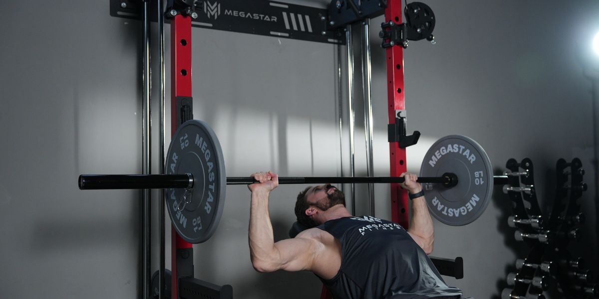 A person performing a barbell bench press exercise with a MEGASTAR barbell, using 10 lb weights, on a red MEGASTAR rack in a gym setting.