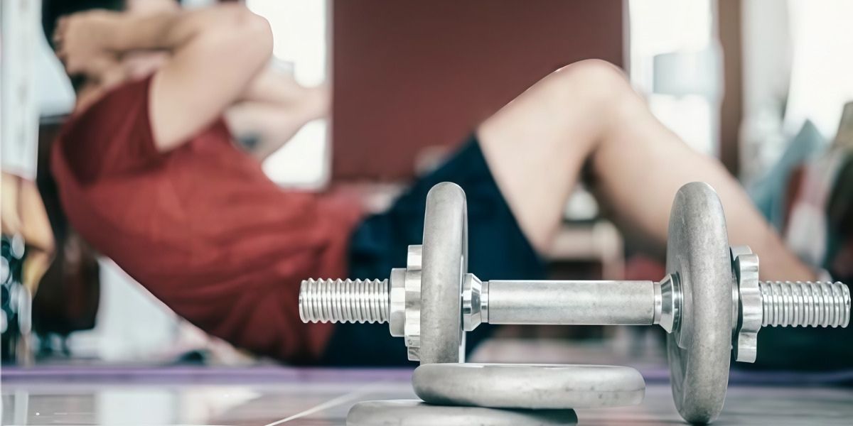 Close-up of an adjustable dumbbell and plates with a person doing sit-ups on a mat—ideal for Strength Training Workouts at Home.