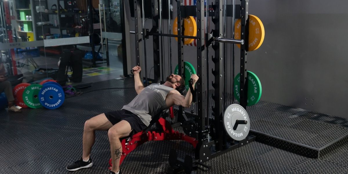 Athlete performing incline cable fly on an adjustable weight bench inside an all-in-one Smith machine functional trainer in a gym.