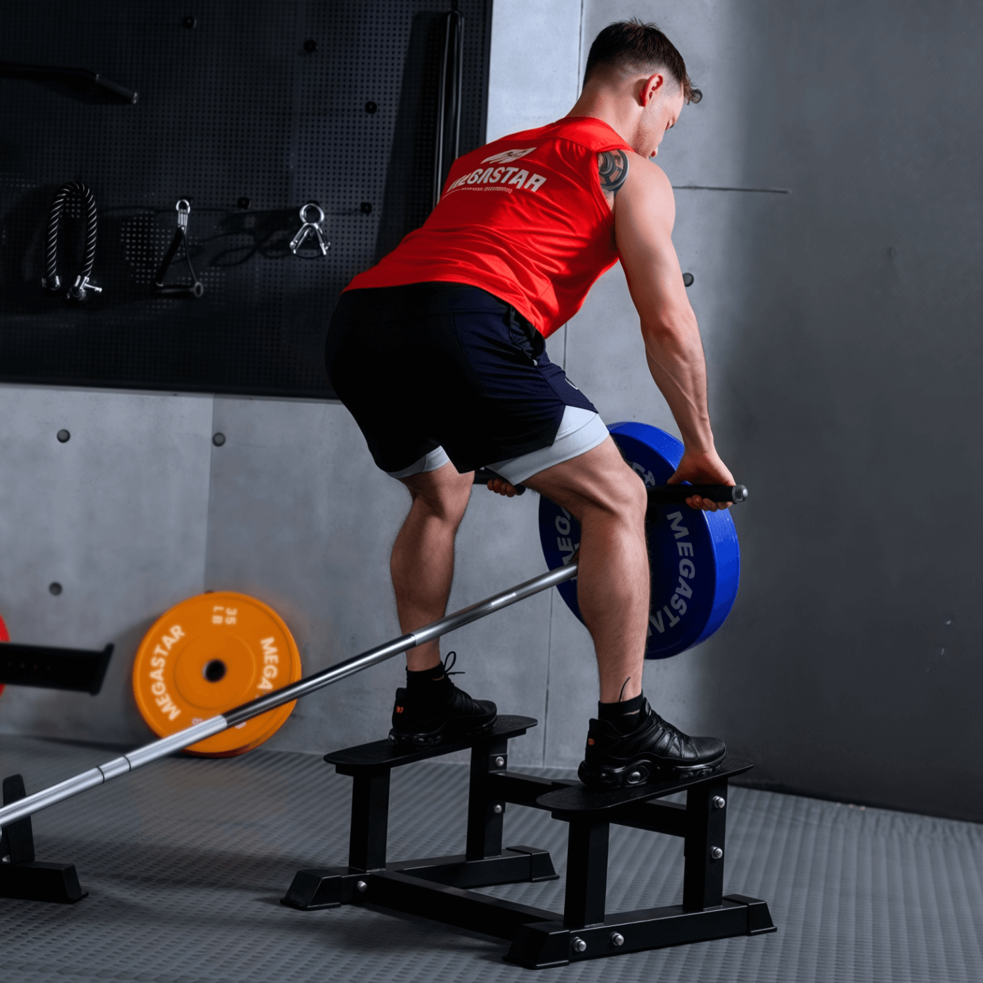 A person performing T-Bar rowing on the MEGASTAR T Bar Rowing Platform, using a barbell with a blue MEGASTAR weight plate.