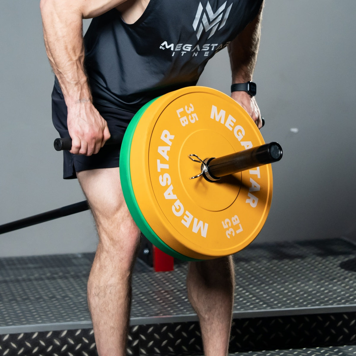 Athlete setting up a landmine row with a barbell loaded with MEGASTAR Bounce Bumper Plates—35 lb orange stacked with green—durable Olympic plates for strength training.