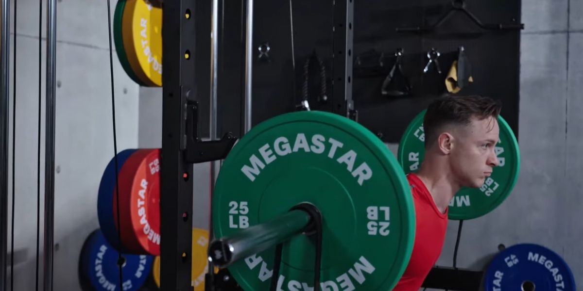 Athlete performing a barbell squat on a Megastar Power Rack, using green 25 lb MEGASTAR bumper plates in a home gym setting.